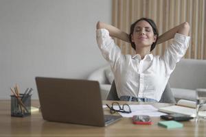 Young happy italian woman with hands behind head relaxing at workplace in home office photo