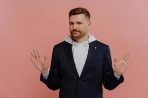 Strict red haired man in casual clothes spreading palms sideways and saying no photo