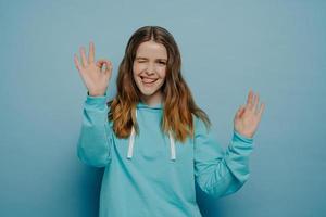 Happy young girl showing okay sign posing over blue blue background photo