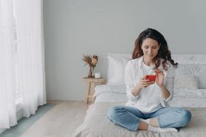 joven mujer bonita está charlando por teléfono en casa. feliz chica europea en ropa casual está enviando mensajes de texto. foto