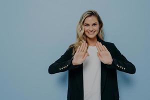 Smiling polite young woman dressed in black blazer over white tshirt keeping hands in stop gesture photo