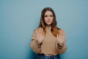 Pretty female demonstrating stop gesture while posing against blue wall photo