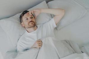Young tired bearded man lying on bed with open eyes photo