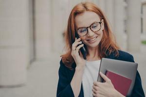 joven mujer de negocios caucásica de 30 años de pie al aire libre y hablando por teléfono inteligente con el cliente foto