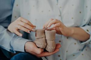 padres esperando bebé. mujer y hombre irreconocibles sostienen botines para recién nacidos. esperar antes del parto. nuevo concepto de familia foto