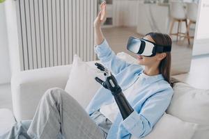 European woman is getting used to modern bionic prosthesis using vr headset. Electronic technology. photo