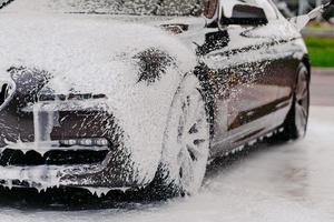 detergente quimico para limpieza de auto. coche en espuma blanca. vehículo de lavado. lavado de autos transporte cubierto con jabón. agua a alta presion foto