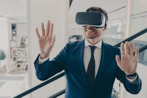 Young excited man office worker using virtual reality simulator at work, moving hands in air photo