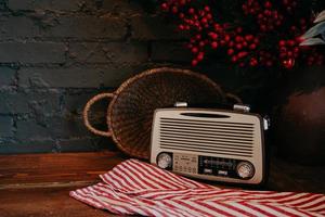 Retro radio on wooden table with wicker basket and floral decor. Vintage style. Antique old broadcast radio receiver on rustic background. photo