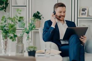 Freelance workday. Cheerful busy man manager works distantly from home online makes video call via laptop computer and headphones discuss working issues with business partner analyzes statistics photo