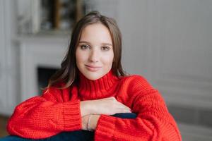 Shot of pleasant looking young brunette girl has good rest at home, looks directly at camera, has healthy skin, spends free time in domestic atmosphere alone. People, beauty, free time concept photo