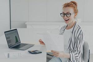 Young redhead woman feeling overjoyed while reading letter with bank notification or news about last mortgage payment photo