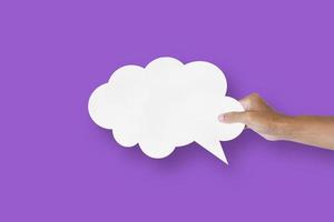 mano que sostiene el globo de la burbuja del discurso de la forma de la nube del papel blanco aislado en las burbujas de la comunicación del fondo púrpura foto