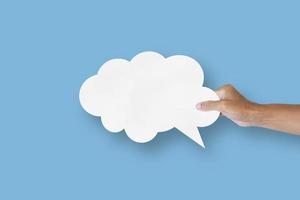 hand holding white paper cloud shape speech bubble balloon isolated on light blue background. photo