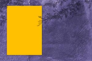 maqueta de afiche cuadrado amarillo vacío con sombra clara sobre fondo de pared de hormigón púrpura. foto