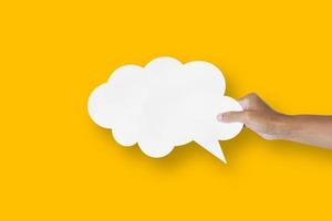 hand holding white paper cloud shape speech bubble balloon isolated on yellow background communication bubbles photo