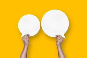 hand holding round white paper balloons speech bubbles isolated on yellow background photo