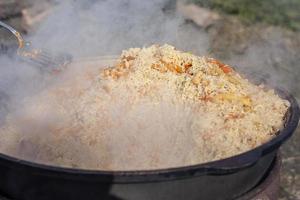 Cook cooks pilaf in a cauldron. Pilaf with vegetables and meat cooked over an open fire. photo