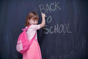 niña de la escuela con mochila escribiendo pizarra foto