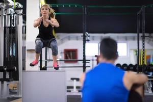 woman working out with personal trainer jumping on fit box photo