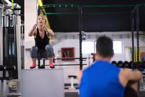 woman working out with personal trainer jumping on fit box photo