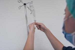 General practitioner holding intravenous drip infusion. Doctor handling IV fluid drip with copy space on white background. Nurse performing Intravenous therapy. photo