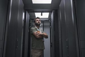 Portrait of male technician or network administrator standing brave as a hero with arms crossed in data center server room. photo