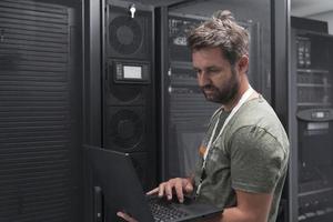 Data Center Engineer Using Laptop Computer Server Room Specialist Facility with Male System Administrator Working with Data Protection Network for Cyber Security or Cryptocurrency Mining Farm. photo