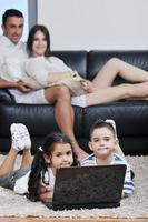 familia joven feliz divertirse y trabajar en la computadora portátil en casa foto