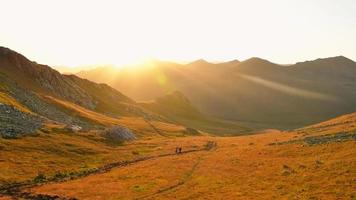 excursionistas de hombre y mujer en la caminata de distancia en el sendero al aire libre en la hermosa puesta de sol en otoño juntos. cámara lenta contra personas activas del sol en caminata en las montañas del Cáucaso video