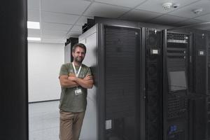 retrato de un técnico o administrador de red masculino que se muestra valiente como un héroe con los brazos cruzados en la sala de servidores del centro de datos. foto