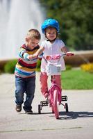 Boy and girl in park learning to ride a bike photo