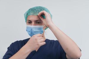 Close up of female doctor or scientist with a medical mask and surgical cap over grey background. She is adjusting mask with photo