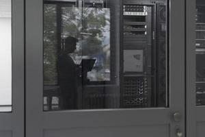 Software Engineer Working on a Laptop Computer in a Modern Server room. Monitoring Room Big Data Scientist in reflection of the entrance door. photo