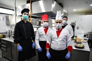 group chefs standing together in the kitchen at restaurant wearing protective medical mask and gloves in coronavirus new normal concept photo