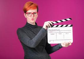 mujer pelirroja sosteniendo la chapaleta de la película sobre fondo rosa foto