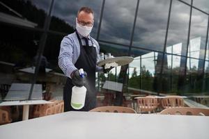 Waiter cleaning the table with Disinfectant Spray in a restaurant photo