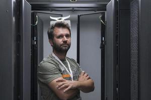 retrato de un técnico o administrador de red masculino que se muestra valiente como un héroe con los brazos cruzados en la sala de servidores del centro de datos. foto