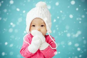 Baby with white poodle hat and knitted mittens with snow falling photo