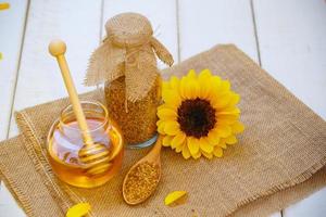 Glass bowls with honey another with pollen. Honey dipper, sunflower on the wooden background photo