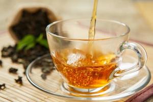 taza de té caliente y hojas de té en un mantel de madera foto