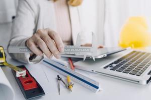 Dos colegas discutiendo el trabajo de datos y una tableta, un portátil con un proyecto arquitectónico en el sitio de construcción en un escritorio en la oficina foto