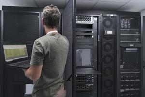 Data Center Engineer Using Laptop Computer Server Room Specialist Facility with Male System Administrator Working with Data Protection Network for Cyber Security or Cryptocurrency Mining Farm. photo