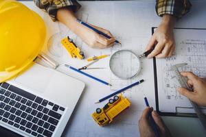 Dos colegas discutiendo el trabajo de datos y una tableta, un portátil con un proyecto arquitectónico en el sitio de construcción en un escritorio en la oficina foto