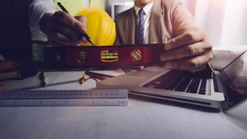 Two colleagues discussing data working and tablet, laptop with on on architectural project at construction site at desk in office photo
