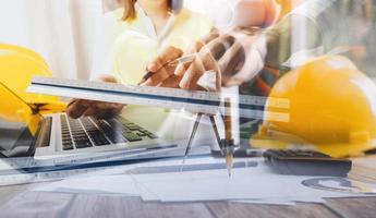 Two colleagues discussing data working and tablet, laptop with on on architectural project at construction site at desk in office photo