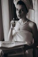 Beautiful young woman in a towel smokes a cigarette and reads newspaper photo