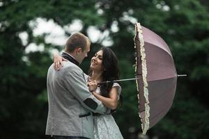 joven y hermosa pareja europea escondiéndose de la lluvia bajo un paraguas foto