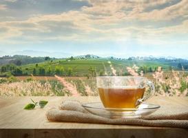 Cup of hot tea with sacking on the wooden table and the tea plantations background photo