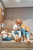 Young happy family with kid unpacking boxes together sitting on sofa photo